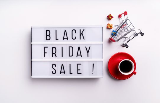 Black Friday shopping sale concept. Black Friday Sale words on lightbox with cup of coffee and shopping cart top view flat lay on white background