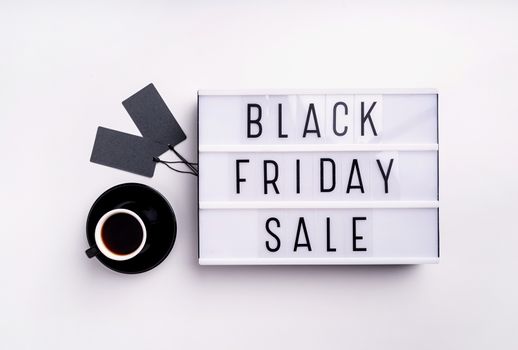Black Friday shopping sale concept. Black Friday Sale words on lightbox with cup of coffee and black price tags top view flat lay on white background