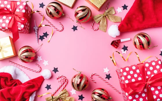 New Year and Christmas flat lay. Top view of christmas and new year decorations with confetti, gift boxes and sants hats on pink backgriund flat lay