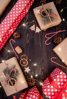 Christmas gifts wrapping. Gift boxes wrappaed in craft paper decorated with pine cones, candy canes and fir tree branches top view flat lay on dark wooden background