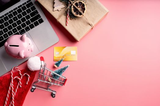 Christmas planing, online shopping concept. Top view of laptop, christmas decorations and piggy bank on pink background, flat lay