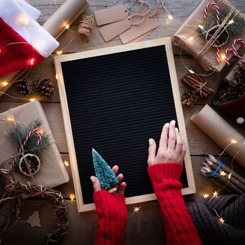 Zero waste and eco friendly christmas concept. Female hands holding blank letter board with christmas gifts and eco friendly decorations top view flat lay