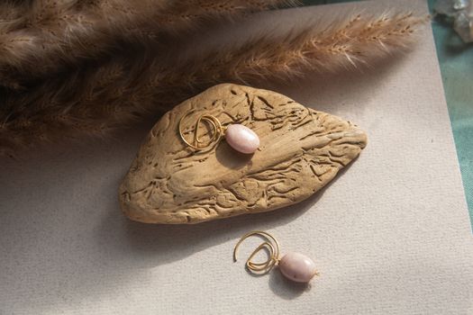 Stylish earrings made of natural pink opal stone with Golden brass fittings on piece of wood pattern from the activity of bark beetle. Natural day solar lighting.