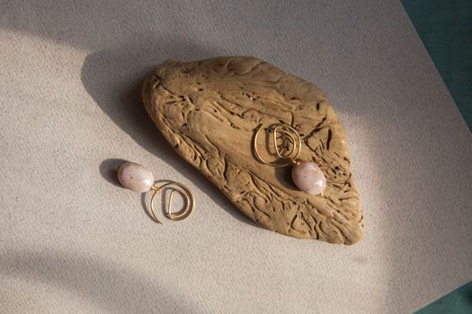 Stylish earrings made of natural pink opal stone with Golden brass fittings on piece of wood pattern from the activity of bark beetle. Natural day solar lighting.
