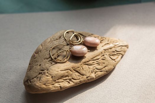 Stylish earrings made of natural pink opal stone with Golden brass fittings on piece of wood pattern from the activity of bark beetle. Natural day solar lighting.