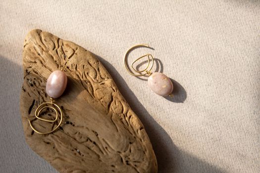 Stylish earrings made natural pink opal stone with Golden brass fittings piece of wood pattern from activity bark beetle. Natural day solar lighting.