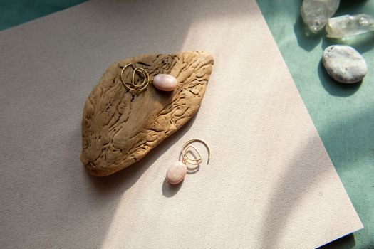Stylish earrings made natural pink opal stone with Golden brass fittings piece of wood pattern from activity bark beetle. Natural day solar lighting.