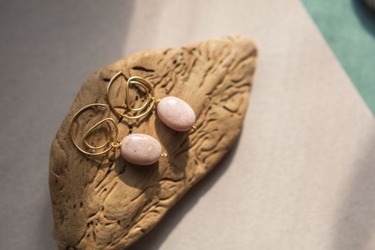 Stylish earrings made natural pink opal stone with Golden brass fittings piece of wood pattern from activity bark beetle. Natural day solar lighting.