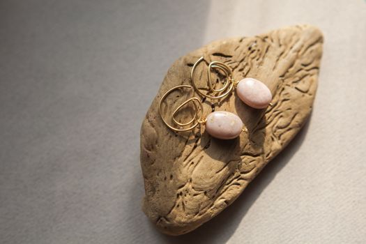Stylish earrings made natural pink opal stone with Golden brass fittings piece of wood pattern from activity bark beetle. Natural day solar lighting.