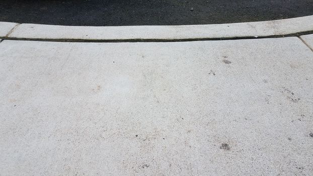 grey cement sidewalk and curb with asphalt or road