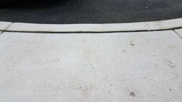 grey cement sidewalk and curb with asphalt or road