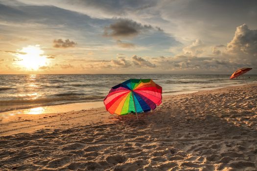 Rainbow umbrella on White sand at Delnor Wiggins State Park at sunset in Naples, Florida.