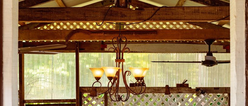 A rustic chandelier hanging from old wooden beams amongst farming objects in a country cafe