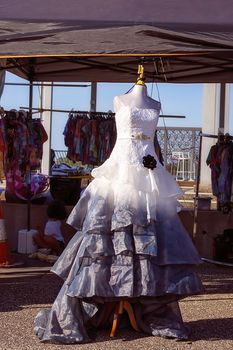 An elegant formal gown with an embroidered bodice and layers of chiffon on the skirt, featuring a beaded belt and a black rose, on sale at a market stall