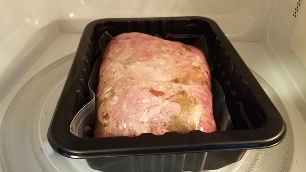 savory red meat pork in plastic bag in container in microwave