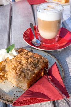 Cup of cappuccino, slice of apple pie with whipped cream on the grey table in cafe. Schwerin cafe. Outdoor.