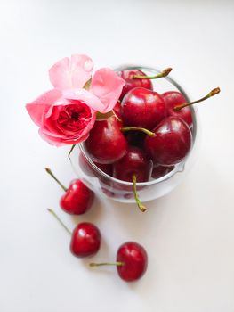 In a glass glass a ripe cherry with a rose flower isolated on a white background