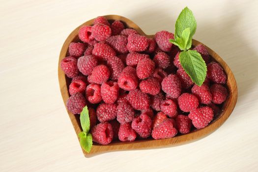 A large handful of raspberries in a wooden heart shaped container