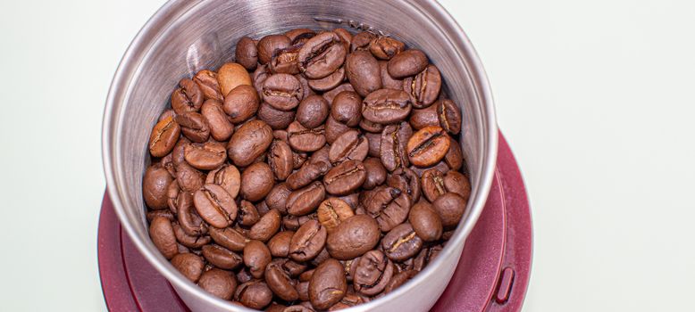 A lot of coffee beans in a metal coffee grinder on a white background. Isolated coffee items