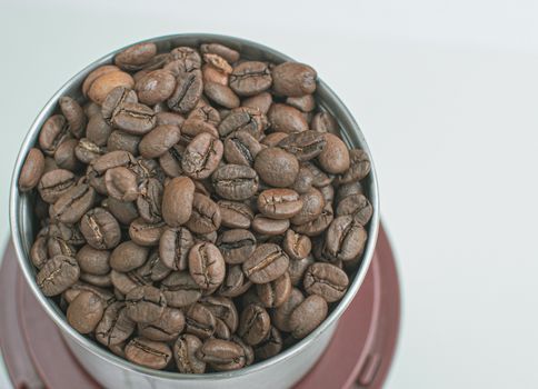 A lot of coffee beans in a metal coffee grinder on a white background. Isolated coffee items