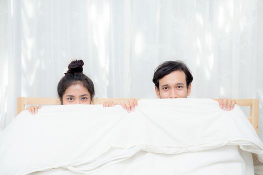 Asian young lovely couple sitting in a bed, happy smile looking at camera, cover under blanket.