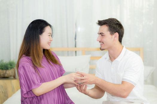 Asian handsome husband takes care about pregnant woman with gives a glass of milk lovely pregnant.