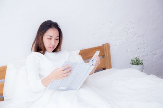 Asian woman reading a book and smiling in bedroom. lifestyle concept.