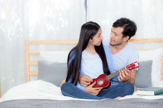 Young Asian couple playing ukulele relaxing with happiness and joyful in bedroom.