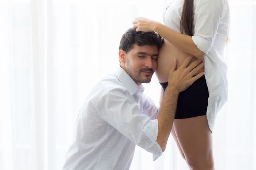 Asian man father ear listening to the belly of the pregnant wife to the movements of the child.