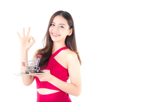 Smiling asian woman in red dress holding tablet with glad girl gesture ok and cart on tablet isolated on white background.