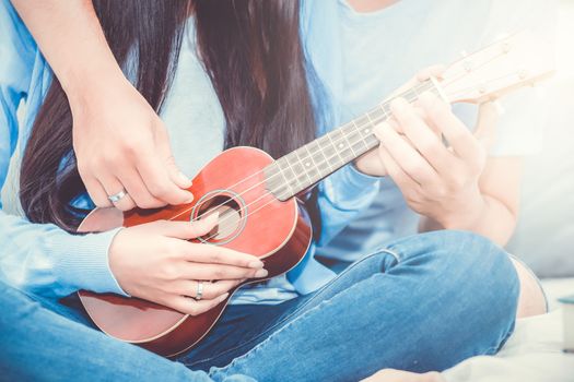 Young Asian couple playing ukulele relaxing with happiness and joyful in bedroom.