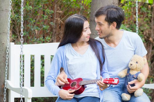 Young asian woman and man couple sitting at park playing ukulele and sing a song outdoors relax concept.