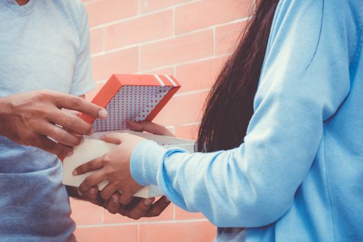 Asian couple young man giving gift to woman outdoors. Happy family concept.