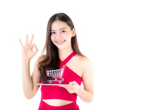 Smiling asian woman in red dress holding tablet with glad girl gesture ok and cart on tablet isolated on white background.