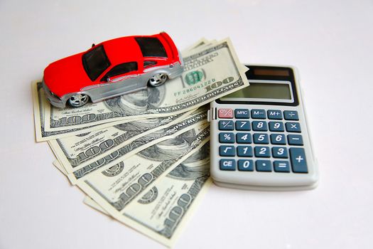 The red car is on dollars spread out on a white table next to the calculator.Texture.Background.