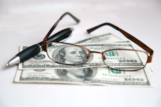 Glasses in a frame are on dollars with a black pen on a white table.Texture.Background.