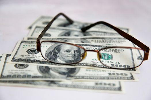 Glasses in a frame lie on dollars spread out on a white table.Texture.Background.