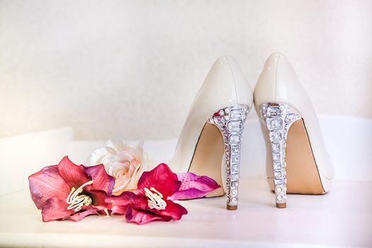Wedding high-heeled shoes stand on a mirrored table next to the red flowers