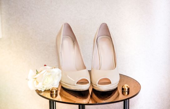 Shoes beige high-heeled stand on a mirrored table next to a rosebud
