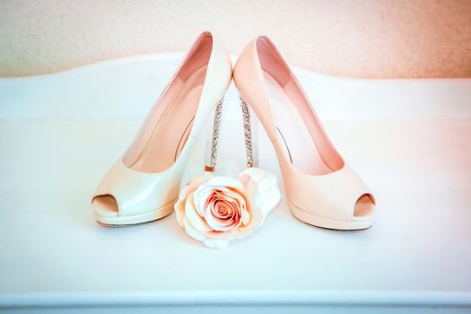 High-heeled shoes stand on a white chest of drawers with a rosebud beige