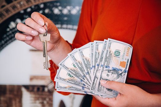 A woman in a red blouse is holding American dollars in her hand with a fan and the keys to the apartment