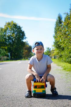 Preschool boy in summer playing alone on the road with a big truck