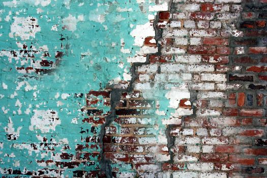 The old cracked wall is made of red brick and smeared with green and white paint