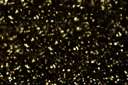 On the surface a large number of defocused round shiny gold sequins on a black background.Texture or background