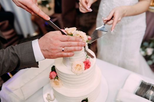 Newlyweds cut together a large and beautiful cake into pieces