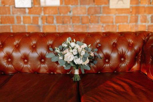 Beautiful wedding bouquet with roses placed on a leather sofa