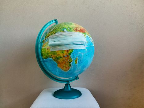 A disinfecting face mask is put on the blue globe of the planet Earth.Texture or background