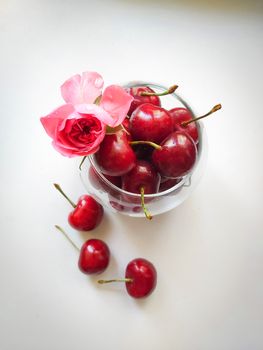 Cherry in a glass glass with a rose flower isolated on a white background
