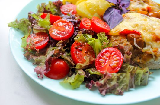 On a white plate a dish of meat with slices of potatoes and cherry tomatoes