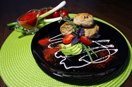 A decorated dish with fried cutlets tomatoes and zucchini slices is served